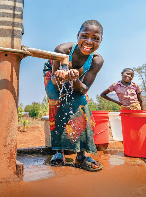 Two smiling girls collect water while at a waterpoint in Malawi